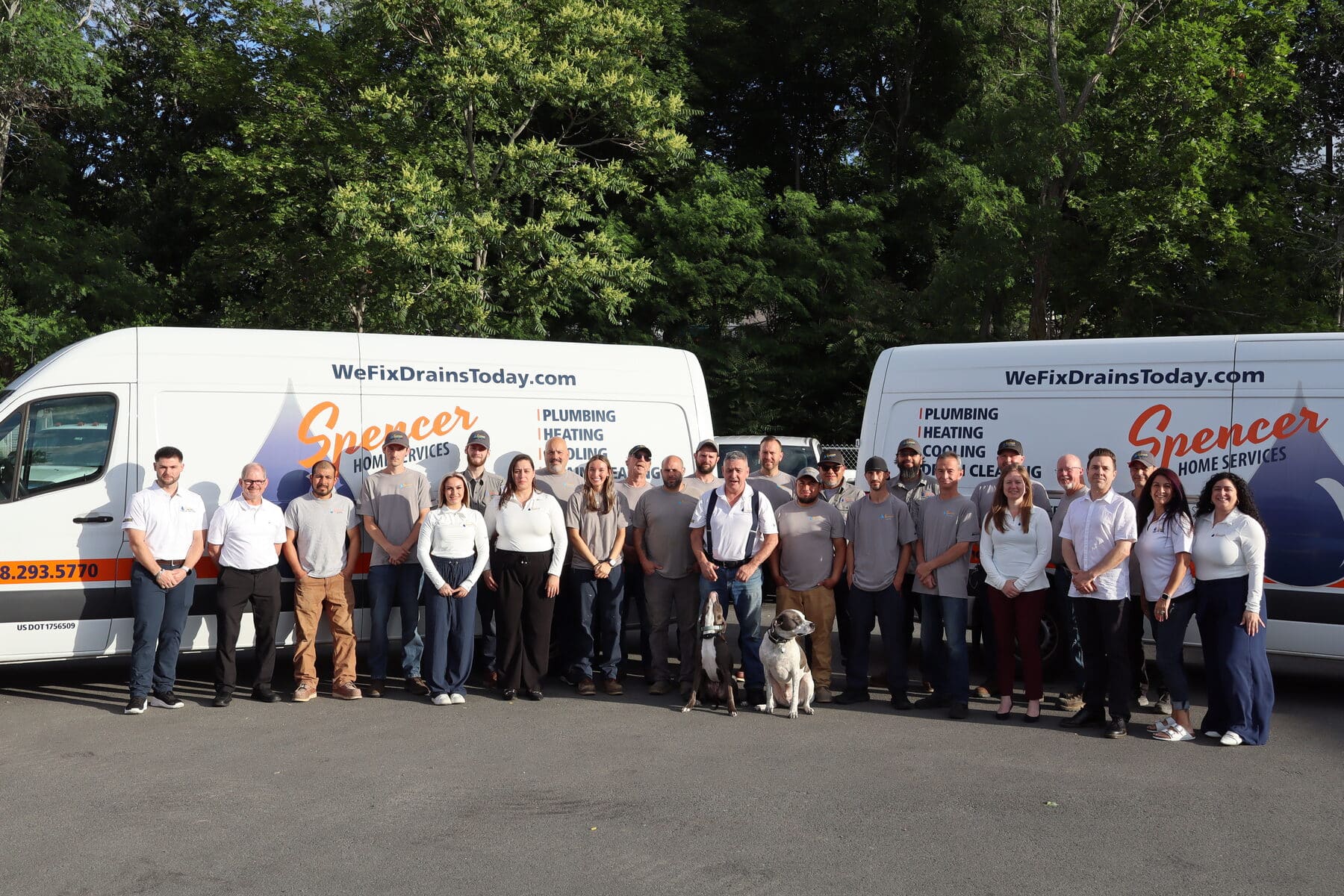 The Spencer Home Services team with two dogs in front of branded plumbing, heating, cooling and drain service vans at the Peabody, Massachusetts headquarters